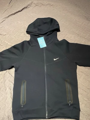 Svart Nike NOCTA hoodie med dragkedja - Snygg svart hoodie från Nike NOCTA-kollektionen med hel dragkedja framtill, två fickor med dragkedja och huva. Diskret Nike Swoosh på bröstet och NOCTA-detaljer på ryggen och ärmen. Tillverkad i mjukt material som känns lyxigt och modernt. Kan passa S också