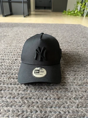 Svart New Era Yankees keps - Snygg svart keps från New Era med 3D-broderad New York Yankees-logga framtill. Justerbar passform med klassisk böjd skärm och mesh på sidorna för extra ventilation. Perfekt för en sportig och trendig look.