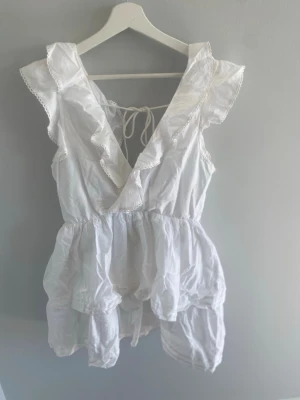 nelly perfect frill dress - Söt vit kortklänning med volangdetaljer och omlott framtill. Klänningen är ärmlös, har v-ringning och knyt i ryggen. Perfekt för sommardagar och har en luftig, lätt passform. öppen rygg. använd 1 gång på skolanavslutning, pris går att diskutera 