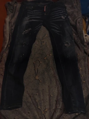 Svarta distressed jeans från Dsquared2 - Säljer ett par svarta jeans från Dsquared2 med slitningar och hål för en riktigt edgy look. Jeansen har skinny fit och coola detaljer som synliga sömmar och tvättade partier. Perfekta för dig som vill sticka ut med din stil.