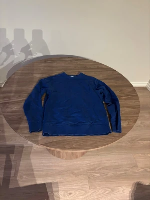 Blå sweatshirt med rund hals - En enkel och stilren blå sweatshirt med rund hals och långa ärmar. Tröjan har ribbade muddar vid ärmslut och nederkant, perfekt för en avslappnad look. Passar till jeans eller mjukisbyxor för en chill outfit.