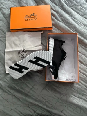 Svarta sneakers med vit sula - Snygga svarta sneakers med en unik, räfflad vit och svart sula som har ett grafiskt mönster undertill. Ovandelen är i textil med strumpliknande passform och svarta snören. Kommer i originalkartong och dustbag. Pris kan diskuteras 