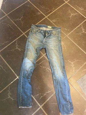 Blå slim fit jeans med slitningar - Snygga blå slim fit jeans med lätt slitna detaljer och klassisk femficksdesign. Jeansen har normal midja och raka ben, perfekta för en avslappnad och trendig look. Tillverkade i denim med en tvättad finish för extra karaktär.