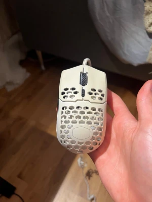 Vit gamingmus med hål - Säljer en vit gamingmus med honeycomb-design och sladd. Musen har en lätt och ventilerad konstruktion med hexagonformade hål på ovansidan och sidorna. Scrollhjulet är svart och musen är ergonomiskt formad för gaming.
