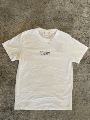 Maison Margiela T-shirt - Säljer denna fina helt oanvända vita tröjan med  MM6 tryck. Tröjan är i storlek M. Men lite liten i storleken så passar nog mest S. Köpt från Vinted. Perfekt nu inför sommaren! Hör av er ifall ni har några frågor! ⚜️⭐️⛱️