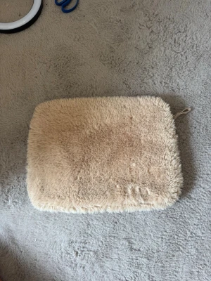 Beige fluffig datorväska - Säljer en beige datorväska med mjukt, fluffigt tyg på utsidan och slät insida. Väskan har dragkedja och är perfekt för dig som vill ha en mysig och unik look till din laptop. Passar till de flesta laptops och är lätt att bära med sig.