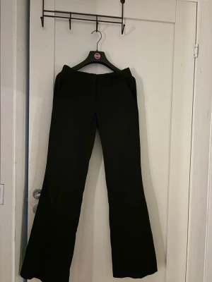 Svarta utsvängda kostymbyxor - Snygga svarta kostymbyxor med utsvängda ben och klassisk passform. Byxorna har fickor fram och hällor för skärp. Perfekta för en stilren look och passar till många olika outfits.