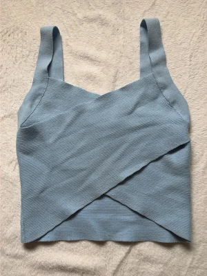 Ljusblå ribbad crop top - Vero Moda - Mjuk ljusblå crop top med breda axelband och ribbad struktur. Toppen har en snygg omlott-design framtill och är tillverkad i ett stretchigt, mjukt material som sitter skönt på kroppen. Perfekt att matcha med höga jeans eller kjol. Bara använd en gång!💕