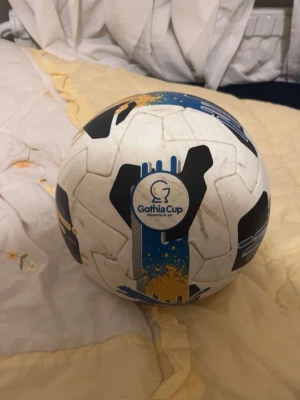 Vit och blå Gothia Cup fotboll - Säljer en vit fotboll med blå, svarta och gula detaljer från Gothia Cup. Bollen har FIFA Quality PRO , jag fick den här bollen efter jag gjorde 3 mål i semifinalen , den är äkta kan har några enstaka repor .