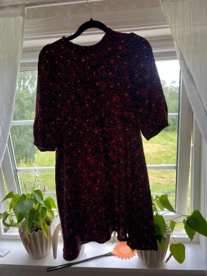 Svart röd klänning med hjärtan  - Kort klänning med svart bas och små röda hjärtan. Modellen har halvlånga ärmar och rund halsringning. Perfekt för dig som gillar en söt och trendig look med hjärtan som mönster.
