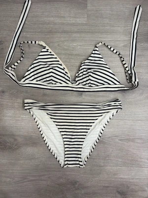 Randig bikini med knytband - Snygg bikini med svartvita ränder. Överdelen har trekantskupor och knytband i nacken och ryggen. Underdelen är klassisk med medelhög midja. Perfekt för stranden eller poolen!