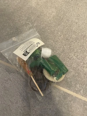 Miniatyrset till dockhus - Ett miniatyrset med små tillbehör till dockhus, inklusive en grön vattenkanna, en brun kratta, en vit hink och en liten kvast. Allt ligger i en genomskinlig plastpåse. Perfekt för dig som gillar att pyssla med dockhus eller miniatyrvärldar.