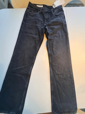 Svarta  jeans med låg midja - Snygga svarta jeans med wide leg passform och låg midja. Klassisk femficksmodell med bälteshällor och knappgylf. Jeansen är nya med lappar på aldrig använda. Jenssen har en stilren look och är tillverkade i denim, perfekt för en trendig vardagsstil. Midjemått 33cm i halvmått, ben innerlängd 82cm