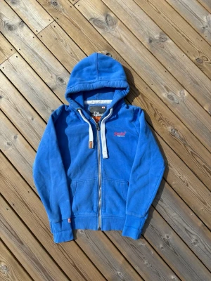 Superdry zip hoodie  - Säljer denna Superdry zip hoodie i mycket bra skick. Storlek L men sitter mer som S/M. Passar perfekt för dig som är mellan 165-172! Hör av er vid frågor eller minsta fundering 🙌  Längd: 60 cm  Bred: 46,5 cm  Ärm: 62 cm