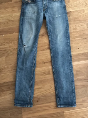 Blå slitna skinny jeans - Säljer ett par blå skinny jeans med slitningar och lätt tvättad look. Jeansen har klassisk femficksdesign och smal passform. Materialet är denim i bomull. Perfekta för en avslappnad och trendig stil.