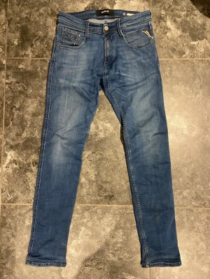 Blå jeans från Replay - Snygga blå jeans från Replay med klassisk femficksdesign och dragkedjedetalj på ena fickan. Jeansen har en smal passform och är tillverkade i stretchigt denimtyg för extra komfort. Perfekta för en trendig och avslappnad look.