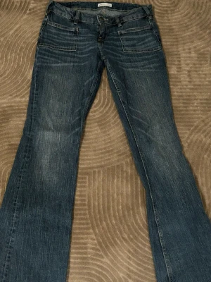 Blå bootcut jeans med fickor fram - Ett par klassiska blå bootcut jeans med två stora fickor fram och två bak. Jeansen har en lätt tvättad look och normal midja. Tillverkade i denim med snygga sömmar och bälteshällor. Perfekta för en avslappnad och trendig stil.