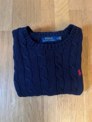 Polo Ralph Lauren Cable Knit – Marinblå | Strl M - Klassisk marinblå Polo Ralph Lauren Cable Knit med röd broderad logga. En tidlös och stilren stickad tröja som passar både vardag och finare tillfällen. ✔️ Mycket fint skick ✔️ Storlek M ✔️ Klassisk passform ✔️ Mjuk och skön kvalitet Finns även i grå – se gärna mina andra annonser. Paketpris vid köp av båda.