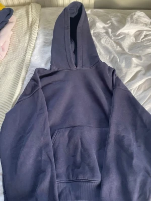 Mörkblå hoodie med magficka - En enkel och stilren mörkblå hoodie med stor huva och rymlig magficka. Hoodien har ribbade muddar vid ärmslut och nederkant. Perfekt för dig som gillar en avslappnad och bekväm look. Materialet känns mjukt och passar till alla tillfällen.