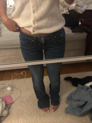 Mörkblå bootcut jeans med låg midja - Säljer ett par mörkblå bootcut jeans med låg midja och klassiska fem fickor. Jeansen har en snygg tvätt och sitter tajt över låren för att sedan bli vidare nedtill. Perfekta för en trendig och avslappnad look.
