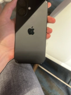 Svart iPhone med dubbla kameror - Säljer en svart iPhone med stilren design och dubbla kameror på baksidan. Telefonen har en slät glasbaksida och den klassiska Apple-loggan. Skärmen täcker hela framsidan och har Face ID. Perfekt för dig som gillar snygg och modern teknik.