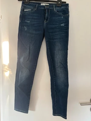 Blå jeans från Zara Z1975 - Säljer ett par blå jeans från Zara Z1975 Denim med klassisk femficksmodell och lätt slitna detaljer framtill. Jeansen har en rak passform och är tillverkade i ett mjukt denimtyg. Perfekta för en avslappnad och trendig look. Använd enstaka gång 