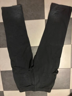 Svarta cargobyxor från New Garments - Snygga svarta cargobyxor från New Garments i storlek XL. Byxorna har raka ben, flera praktiska fickor på sidorna och är tillverkade i ett slitstarkt tyg. Perfekta för en avslappnad och trendig stil.
