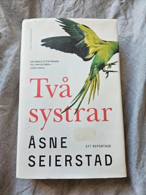 Två systrar av Åsne Seierstad - En fängslande reportagebok av Åsne Seierstad med vit omslag och en grön papegoja på framsidan. Boken handlar om två norska tonårssystrar som radikaliseras och reser till Syrien. Perfekt för dig som gillar verklighetsbaserade berättelser och samhällsfrågor.