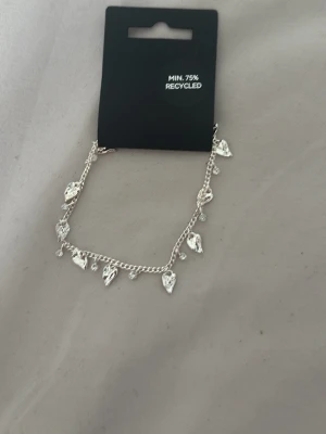 Armband pilgrim - Snyggt armband i silverfärg med små hjärtformade berlocker och pärldetaljer. Tillverkat av minst 75% återvunnet material. Den är helt ny och oanvänd och kostar organellt 449kr