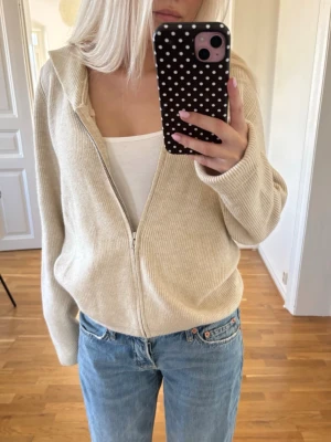 Stickad kofta - Säljer en beige stickad ziptröja🤍. Tröjan har dragkedja framtill, avslappnad passform och långa ärmar. Perfekt att slänga över ett linne eller t-shirt. Använd en gång, skriv för mer info!
