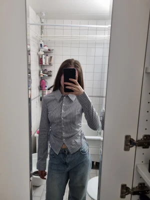 Randig blå och vit skjorta BERSHKA - Säljer en stilren skjorta med smala blå och vita ränder. Skjortan har klassisk krage, knäppning framtill och långa ärmar. Passformen är slim och materialet känns som bomull, perfekt för en clean och fräsch look.