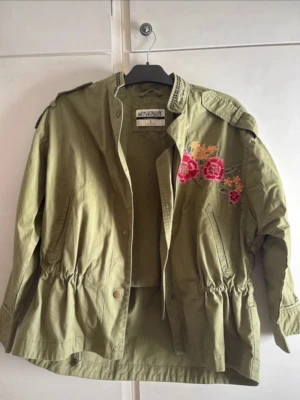 Vårjacka med detaljer  - Snyggaste militärgröna/kakigröna vårjackan med broderade detaljer, med knyte/spänne nere vid midjan. Dvs den är justerbar! Fransk text på baksidan🥰🙏🏻 Passar xs-m!