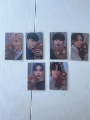 Set med sex K-pop photocard - Säljer ett set med sex photocard med K-pop-idoler som poserar med en brun nallebjörn. Kort i plast med färgbilder, varje kort har unik idol och nalle. Perfekt för samlare eller fans av K-pop och idolmerch.