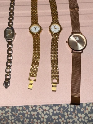 Fyra stilrena armbandsur i metall klockor mix - Säljer fyra snygga armbandsur i olika metallfärger. Två klockor i guld med klassisk länk, en i silver med ovalt ur och en i roséguld med meshband och stenar på urtavlan. Perfekta accessoarer för att lyfta din outfit.