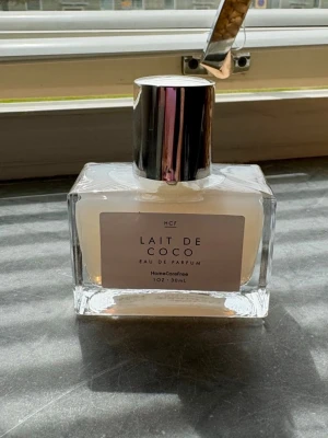 Lait de Coco Eau de Parfum 30 ml - Säljer en stilren parfymflaska med doften Lait de Coco. Flaskan är genomskinlig med en silvrig kork och innehåller 30 ml Eau de Parfum. Etiketten är ljus och minimalistisk, vilket ger ett fräscht intryck. Perfekt för dig som gillar kokosdofter. Ny