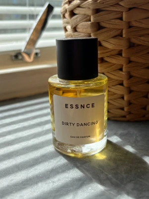 ESSNCE Dirty Dancing Eau de Parfum - En stilren parfymflaska från ESSNCE med doften Dirty Dancing. Flaskan är cylindrisk i genomskinligt glas med svart lock och vit etikett med svart text. Innehållet är gyllengult och ger ett lyxigt intryck. Perfekt för dig som vill ha en unik signaturdoft. Ny 