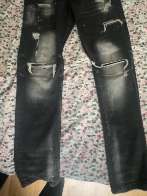 Svarta distressed jeans Supply & Demand - Säljer ett par svarta jeans från Supply & Demand med slitningar, hål och vita färgstänk för en riktigt edgy look. Jeansen har dragkedjedetalj vid fickan och skinny fit. Perfekta för dig som gillar streetwear och vill sticka ut.