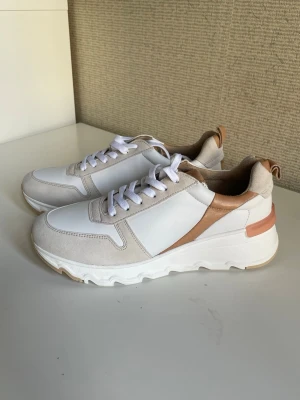 Vita chunky sneakers med beige detaljer i skinn från Tamaris, stl 39 - Snygga chunky sneakers i vitt med beige och ljusbruna detaljer. Ovandelen är i en mix av slätt material och mockaimitation, med vita skosnören och en rejäl sula för extra komfort. Perfekta för en trendig och avslappnad stil. Från Tamaris, stl 39, väldigt bekväma, äkta skinn och mocka detaljer. Nya oanvända. 