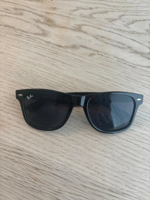 Ray-Ban Justin classic   - Klassiska svarta Wayfarer solglasögon från Ray-Ban med ikonisk form och mörka glas. Snygg och tidlös design som passar till allt. Tillverkade i Italien och har Ray-Ban-logga på linsen och insidan av skalmen.