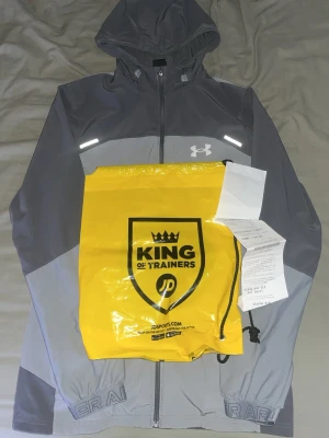Grå vindjacka från Under Armour - Tjena, säljer min under armour vindbreaker. Den har två fickor i fram och samt de vanliga reflexerna som är på dess modeler. Den är bekväm att ha på sig och passar fint. Jag har dustbag och kvitto på den som följer med. Den är i ny skick, när den blev köpt från affär kosta den 1100 därför jag säljer den för 800 eftersom att den knappast är använd och är i riktigt fint skick. Jackan är 100% äkta och kvittot är beviset. Skriv vid minsta fråga, pris kan eventuellt diskuteras men vill helst ha 800. 