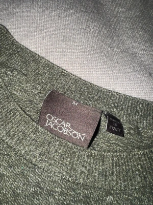 Oscar Jacobson tröja - Mysig grön stickad tröja från Oscar Jacobson med rund halsringning och ribbade muddar. Perfekt för lager-på-lager och enkel att matcha med jeans eller chinos. Tillverkad i Italien för en exklusiv känsla.