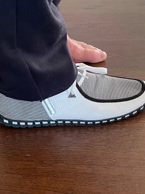 Svartvita loafers med rutmönster - Säljer ett par svartvita loafers med rutmönstrad ovandel och vita snören. Skorna har en kontrasterande svart kant runt öppningen och en sula med vita rutor längs kanten. Materialet ser ut att vara en mix av textil och syntet, perfekt för en avslappnad stil.