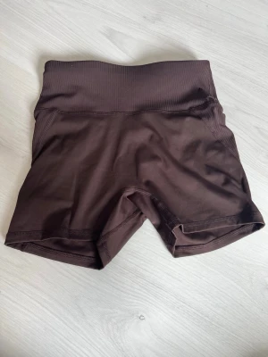Bruna höga cykelshorts - Säljer ett par bruna cykelshorts med hög midja och ribbad linning. Shortsen är tillverkade i ett stretchigt material som passar perfekt för träning eller en aktiv vardag. Snygg och enkel design utan synliga loggor eller mönster.
