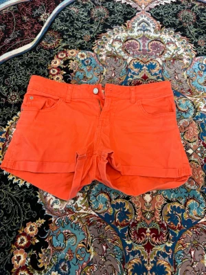 Orange shorts med fickor - Snygga orange shorts med klassisk femficksdesign och uppvikta benslut. De har bälteshällor, knapp och dragkedja framtill. Perfekta för varma dagar och ger en färgklick till din outfit.