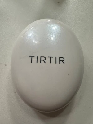 TIRTIR cushion foundation - Säljer en TIRTIR cushion foundation i en oval, vit kompakt dosa med spegel och applikator. Foundationen har en naturlig beige ton och ger ett fräscht, jämnt resultat. Perfekt att ha med i väskan för snabba touch-ups under dagen.