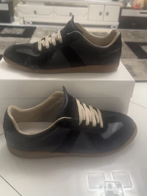 Svarta Margiela GATs - Säljer mina svarta Maison Margiela gats eftersom de inte längre kommer till användning.  Skorna är använda och har ett hål på vänster sko, vilket syns tydligt på bild 4. Utöver det är de i bra bruksskick. Se bilderna för att själv bedöma skicket.  Storleken passar bra för dig som vanligtvis har 46–48.  Priset är inte hugget i sten, så skicka gärna ett bud om du är intresserad. Hör av dig om du har några frågor eller vill ha fler bilder!