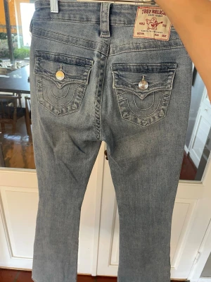 True Religion ljusblå bootcut jeans - Säljer ett par ljusblå bootcut jeans från True Religion, modell BECCA Mid Rise Bootcut. Jeansen har en pytte liten fläck men inget man tänker på så mycket. 