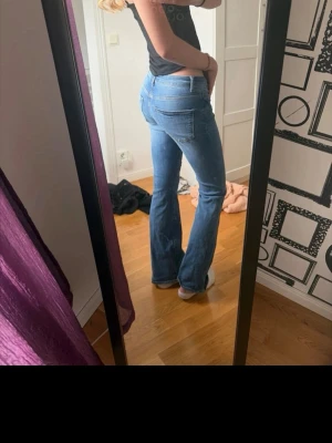 Blå bootcut jeans med låg midja - Säljer ett par snygga blå bootcut jeans med låg midja och klassiska fem fickor. Jeansen har en lätt tvättad look och sitter tajt upptill med utsvängda ben. Perfekta för dig som vill ha en trendig siluett och gillar snygga jeans. Längd 34 stl s 