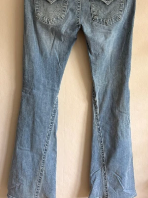 Ljusblå flare jeans Joey true religion  - Säljer ett par ljusblå Joey Low Rise Flare jeans från true religion med snygg utsvängd passform och broderade detaljer på bakfickorna. Jeansen har låg midja och klassisk femficksdesign. Jeansen är lite slitna vid nedre kanten (bild 4) men är i övrigt som nya! 
