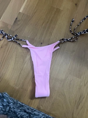 Rosa bikiniunderdel med leopardknyt - Säljer en ljusrosa bikiniunderdel med leopardmönstrade knytband i sidorna. Modellen är smal och har högt skurna ben. Perfekt för dig som vill ha en trendig och djärv look på stranden.
